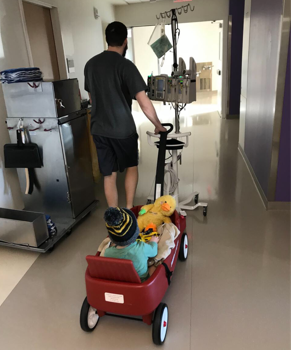 Hudson’s dad pulling him in wagon down hospital hallway.