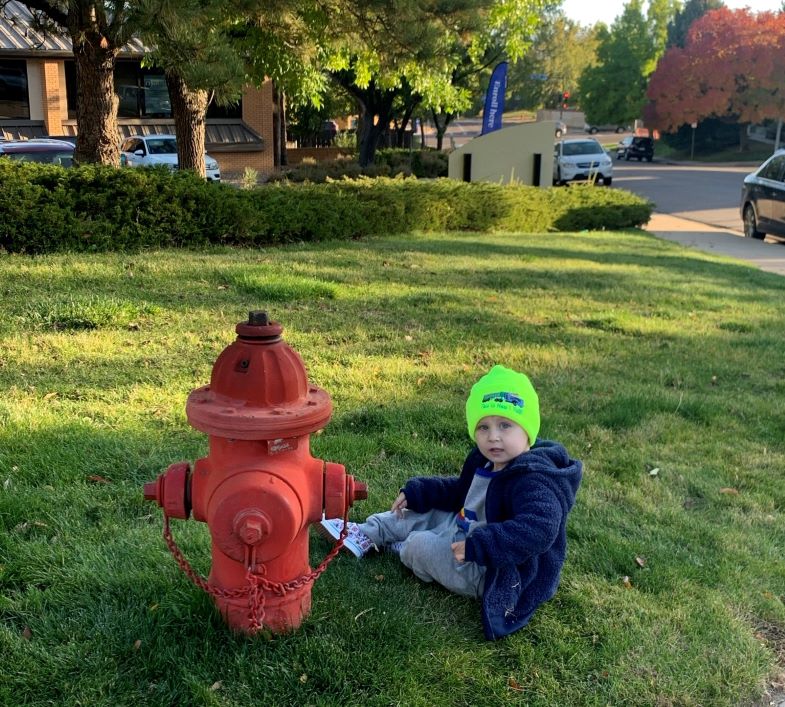 Bodie sitting on ground by fire hydrant.