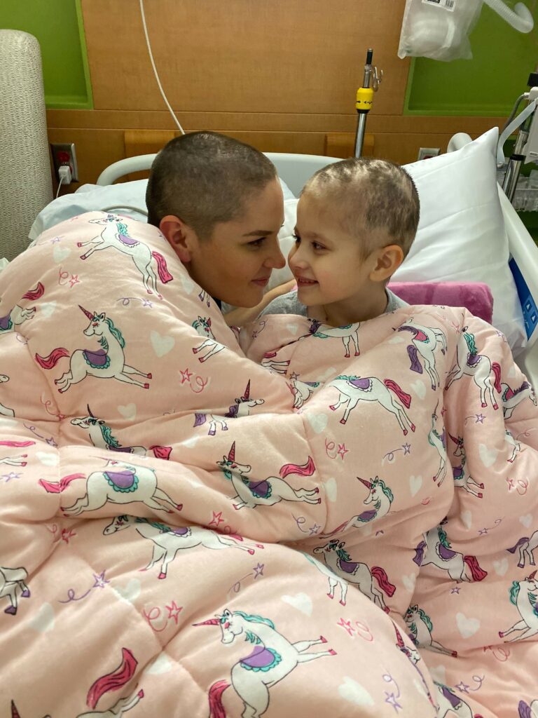 Mia and mom bald in hospital bed.