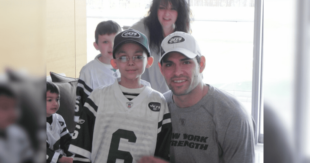 A man and a young boy, both dressed in football gear, pose happily for a photograph, celebrating their shared passion.