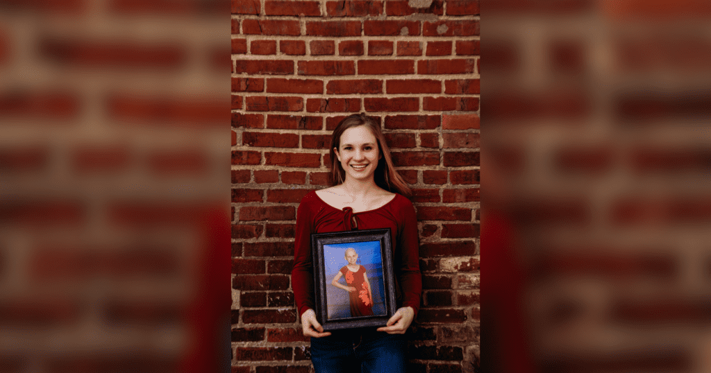 A young woman displays a framed photo of herself, reflecting her individuality and personal journey.