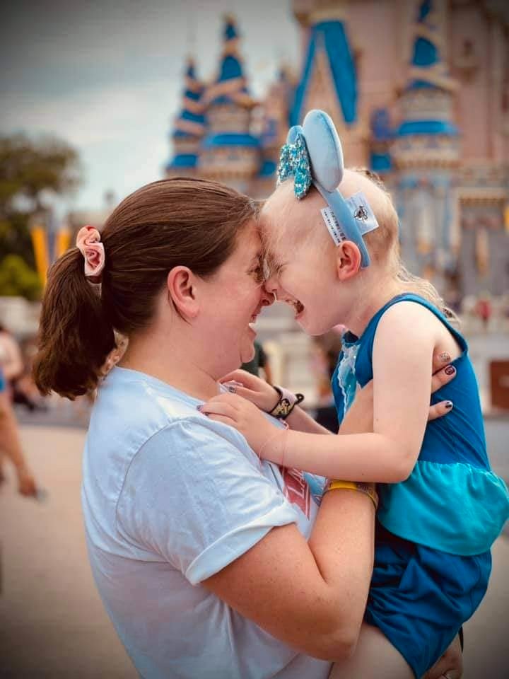 Little girl with cancer hugs her mom at Disneyland.
