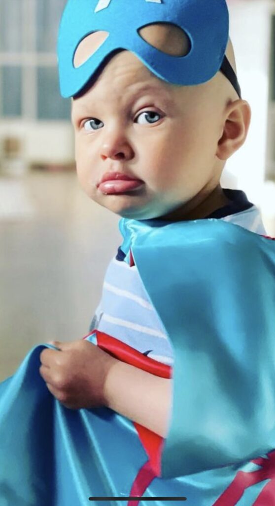Little boy fighting cancer wearing a mask and cape.