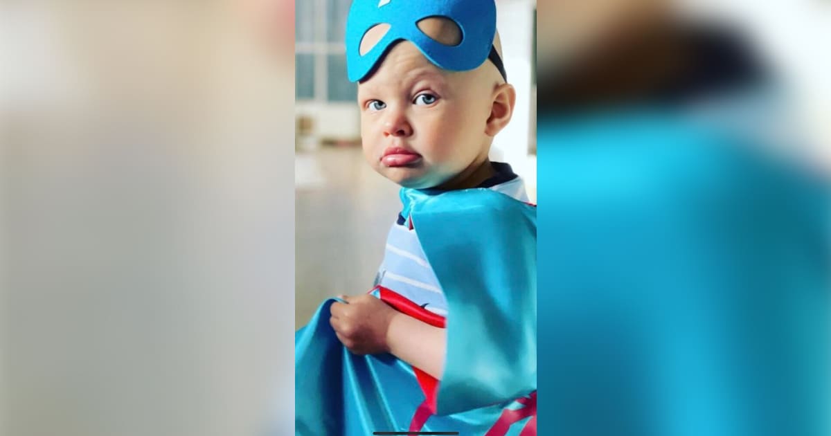Little boy fighting cancer wearing a mask and cape.
