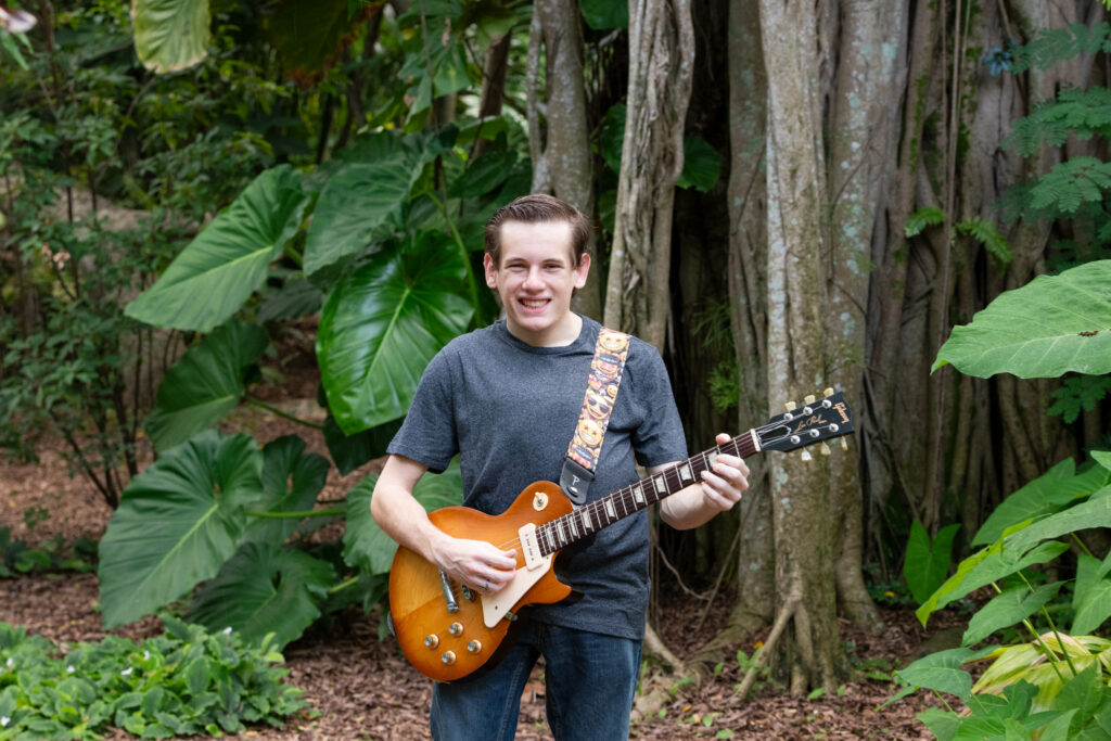 Cancer warrior Aaron holding a guitar with a forest background
