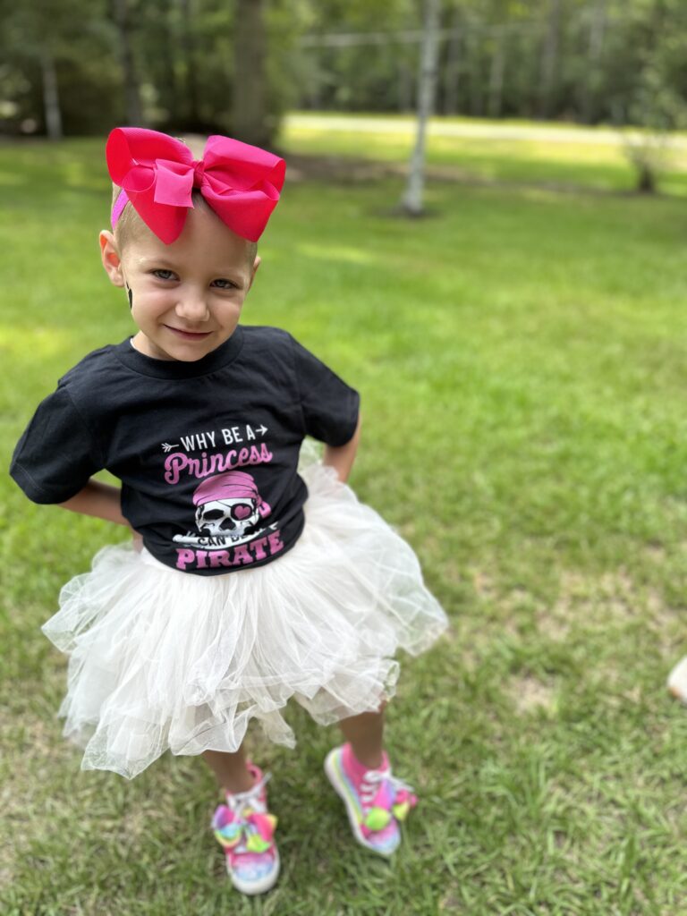 cancer warrior Julianna wearing a 'why be a princess when you can be a pirate' shirt, a tutu, and a headband with a big pink bow