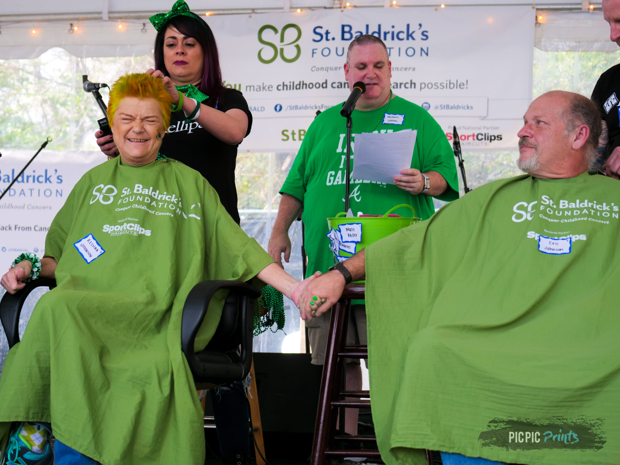 a male and female shavee holding hands while being in the barber chair, getting ready to have their heads shaved
