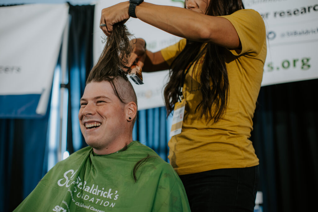 male shavee with his unshaved hair held up by a female barber holding clippers