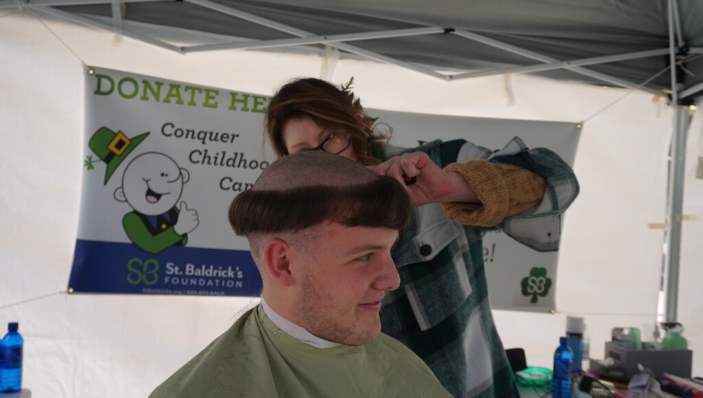 male shavee with the middle of his head shaved a female barber ready to finish it off
