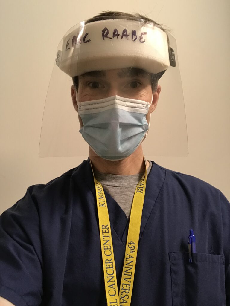Dr. Eric Raabe in navy scrubs, wearing a face mask and a face covering wi the words 'Eric Raabe' on it