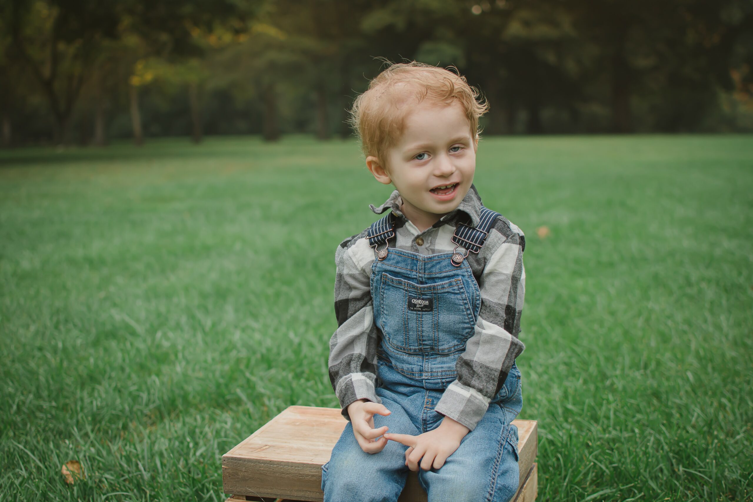 cancer warrior, Sutton, dressed in overalls and sitting on a bench in some grass