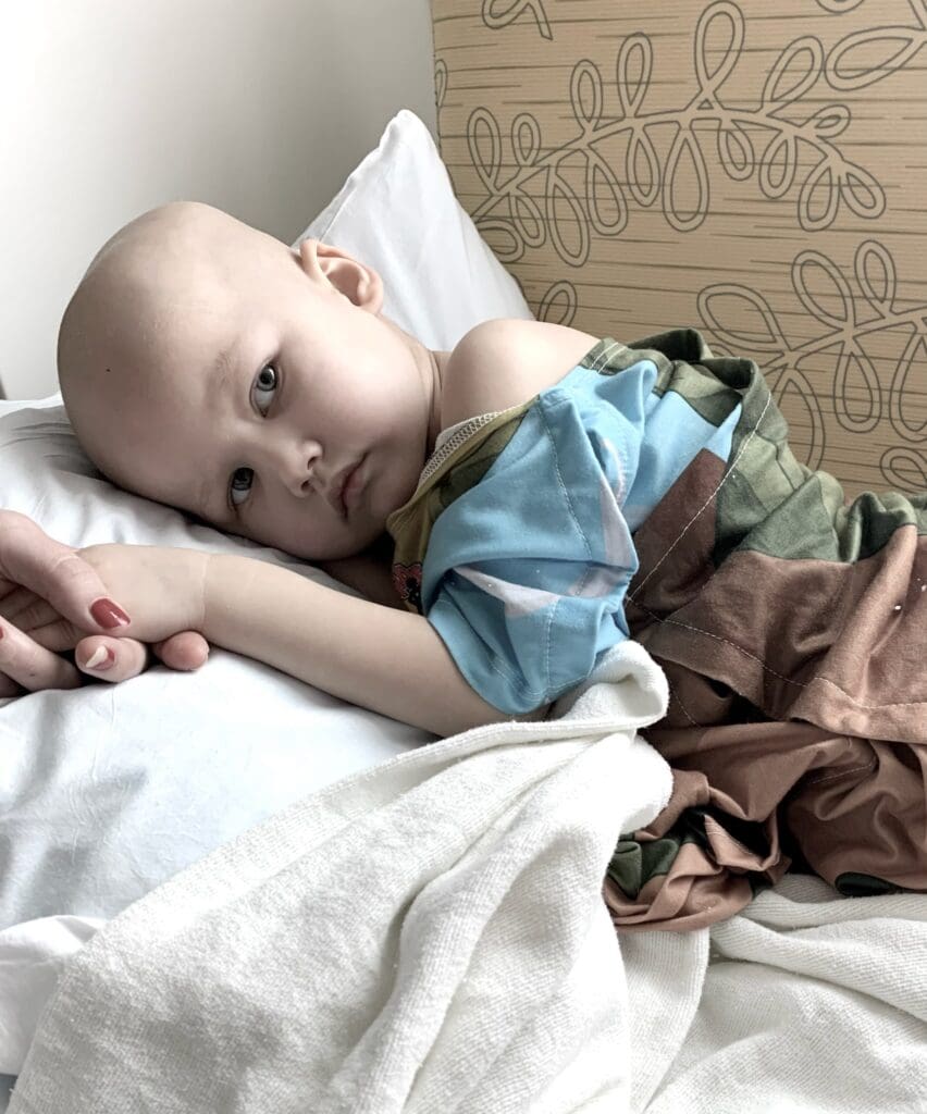 A little girl resting on a pillow, with someone holding her hand