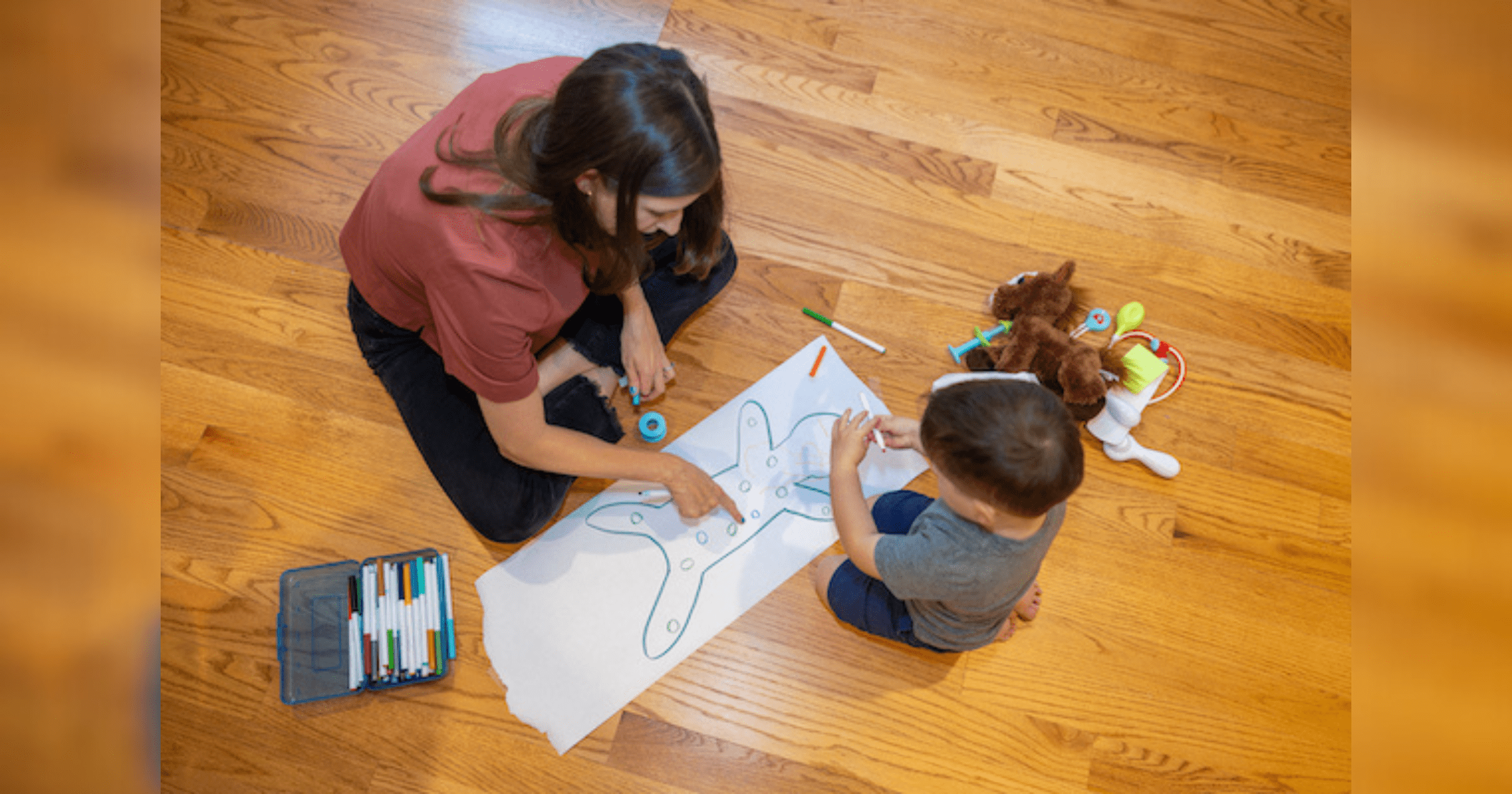 A woman and child sit on the floor, engaged in drawing on paper, showcasing a moment of creativity and bonding.