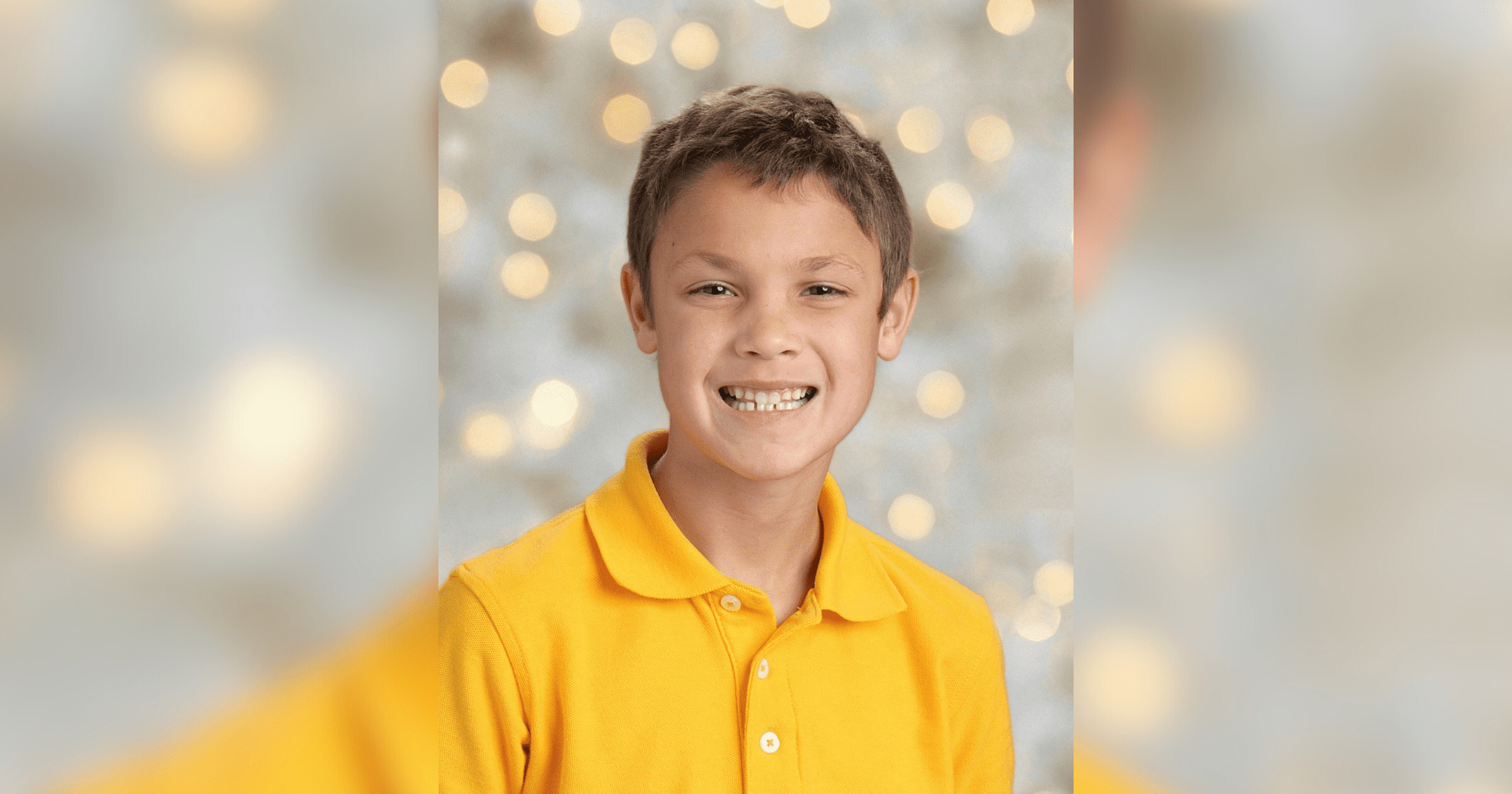 A young boy wearing a yellow shirt smiles brightly, radiating joy and happiness.