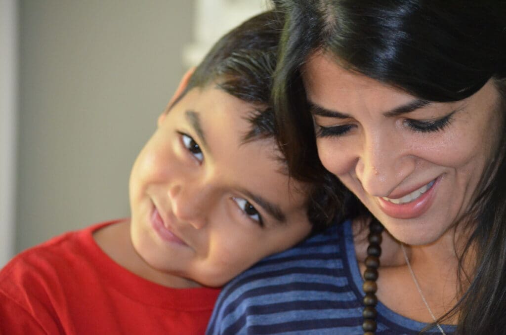 A woman and a child are smiling joyfully at the camera, showcasing a warm and happy moment together.