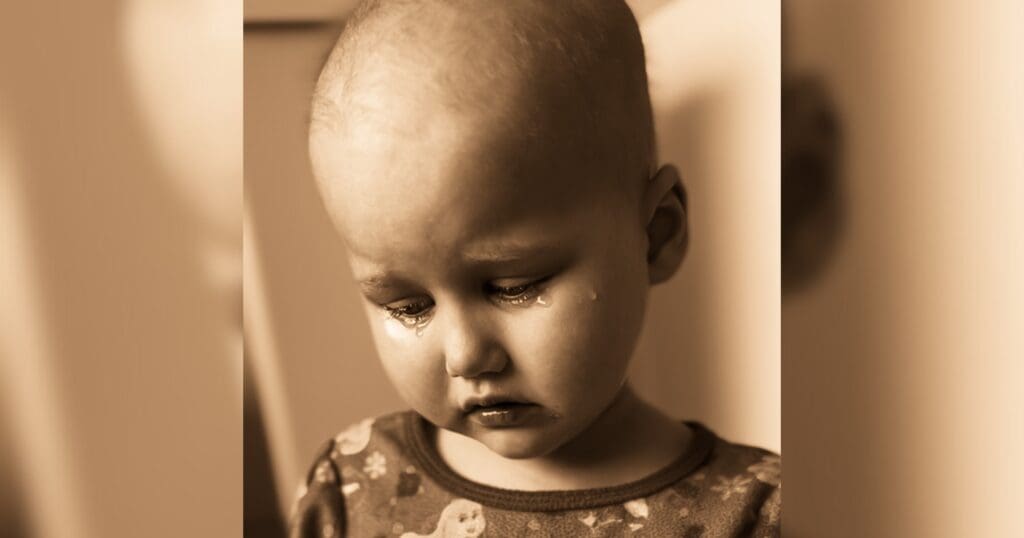 A sad young child with a bald head and tear-streaked face looks down, appearing distressed. The sepia tone evokes a somber, emotional mood.
