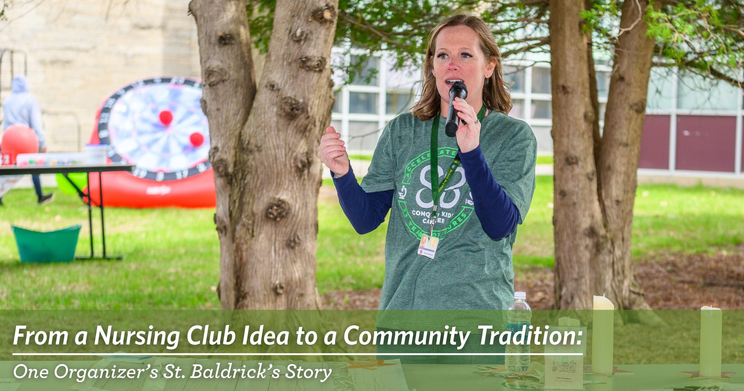 A woman speaks at an outdoor event, holding a microphone. She wears a green St. Baldrick’s t-shirt, standing by a table with candles. A text overlay reads, "From a Nursing Club Idea to a Community Tradition: One Organizer's St. Baldrick's Story." Trees and event setup are visible.