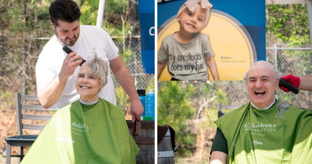 A woman and a man smile while having their heads shaved outdoors, wearing green capes with "St. Baldrick's Foundation." A sign with a child’s photo reads, "My oncologist does my hair," conveying support for cancer awareness.