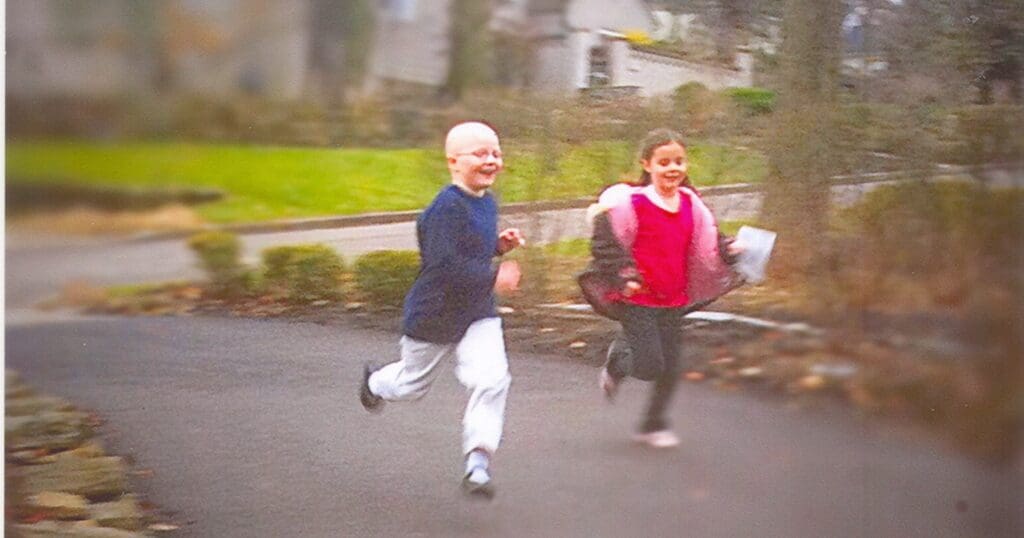 Two girls joyfully run on a path in a garden. One is in a blue top, and the other wears red. The mood is carefree and playful.