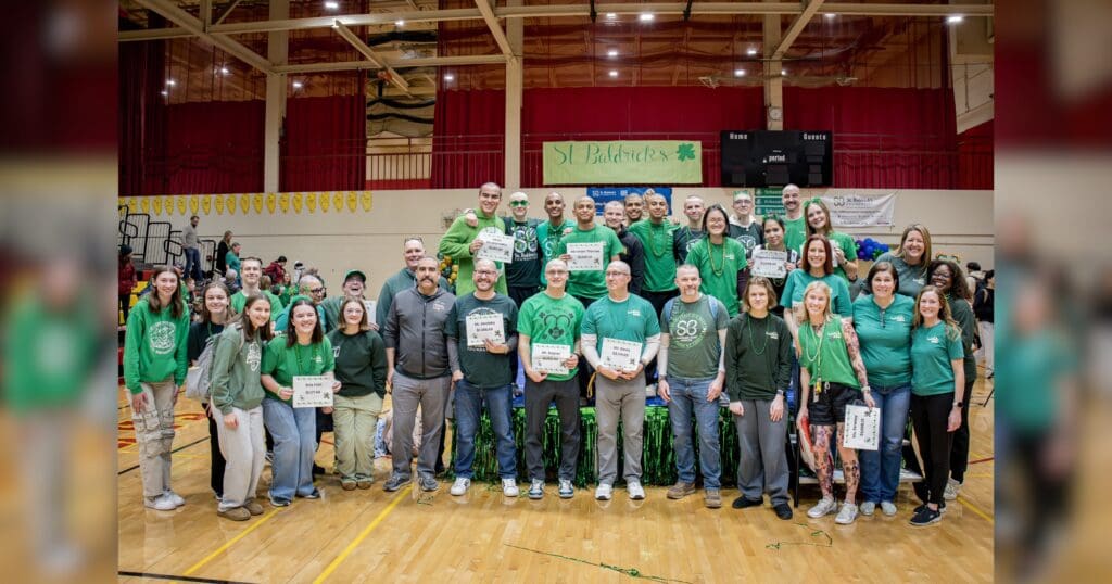A group of individuals wearing green shirts and ties, standing together in a school gymnasium.