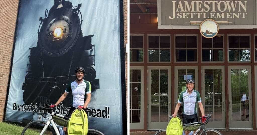 Smiling cyclist poses with a bicycle and bright yellow pannier beside a steam locomotive mural and the Jamestown Settlement entrance.